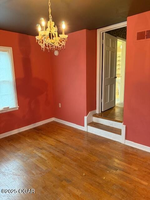 unfurnished room with a notable chandelier, wood finished floors, visible vents, and baseboards