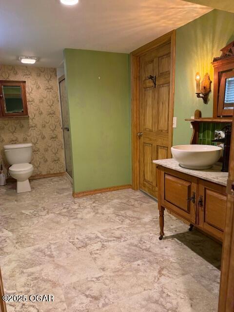 bathroom featuring toilet, wallpapered walls, an enclosed shower, and baseboards