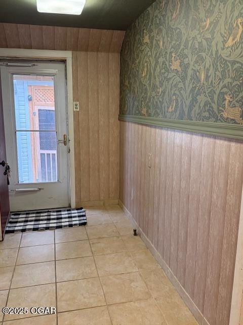 doorway to outside featuring vaulted ceiling, wooden walls, and light tile patterned floors