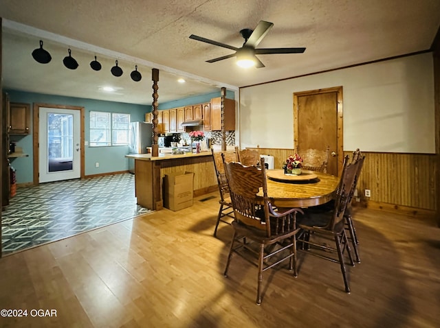 dining room with a textured ceiling, light wood-type flooring, ceiling fan, and wooden walls