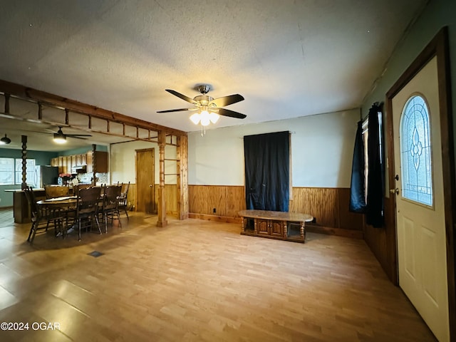 interior space with a textured ceiling, light hardwood / wood-style flooring, ceiling fan, and wood walls