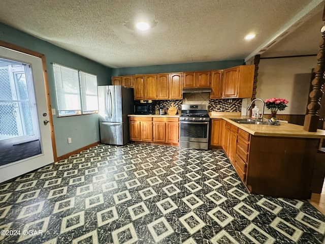 kitchen with decorative backsplash, kitchen peninsula, a textured ceiling, stainless steel appliances, and sink