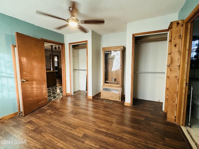 unfurnished bedroom with two closets, ceiling fan, dark wood-type flooring, and a textured ceiling