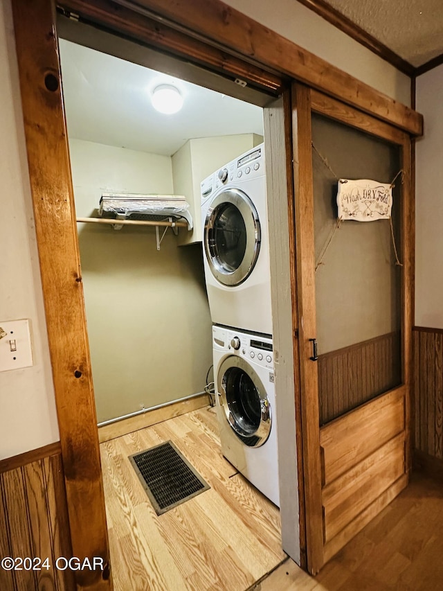 laundry room featuring wooden walls, stacked washer and clothes dryer, and hardwood / wood-style flooring