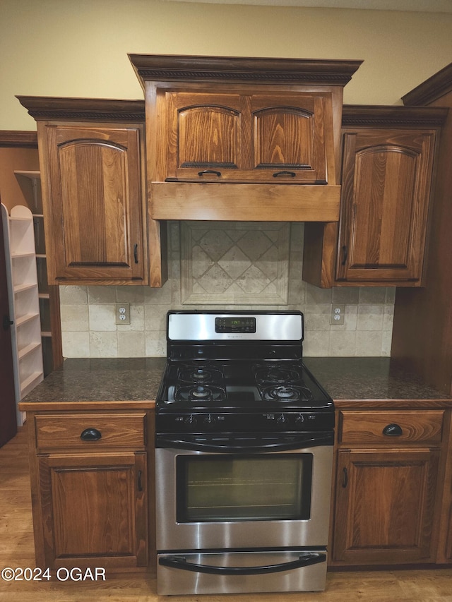 kitchen featuring stainless steel gas stove, decorative backsplash, light wood-type flooring, and range hood