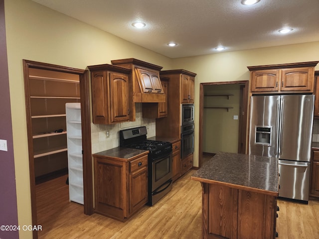 kitchen with decorative backsplash, black appliances, a center island, light wood-type flooring, and a textured ceiling