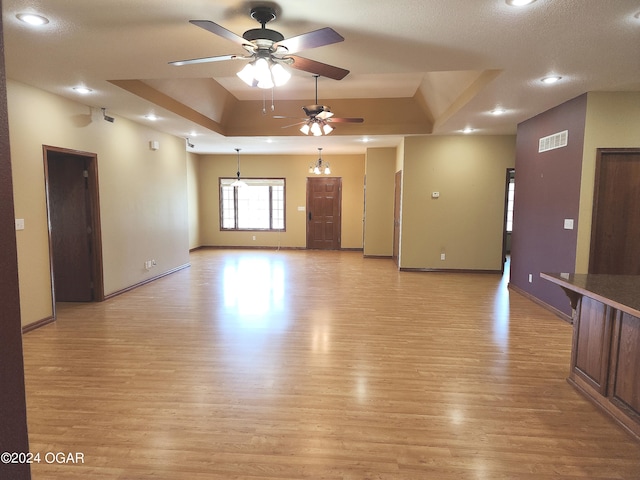 unfurnished living room with light hardwood / wood-style floors, a raised ceiling, a textured ceiling, and ceiling fan