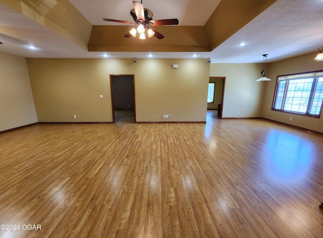 empty room with a textured ceiling, ceiling fan, light wood-type flooring, and a raised ceiling