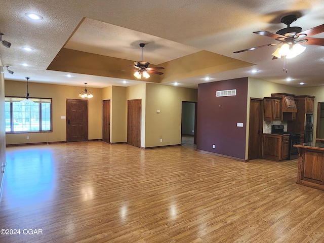 unfurnished living room with ceiling fan with notable chandelier, a textured ceiling, light hardwood / wood-style floors, and a raised ceiling