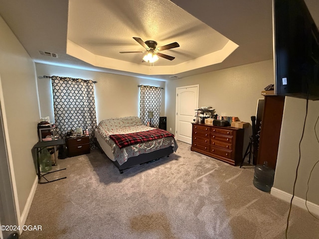 carpeted bedroom featuring a textured ceiling, ceiling fan, and a tray ceiling