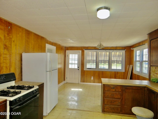 kitchen featuring plenty of natural light, wooden walls, and white appliances