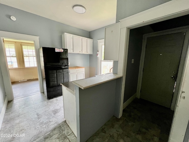 kitchen featuring black refrigerator, white cabinetry, and kitchen peninsula