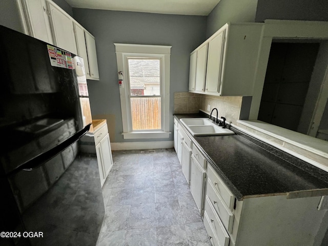 kitchen with black fridge, white cabinetry, sink, and tasteful backsplash