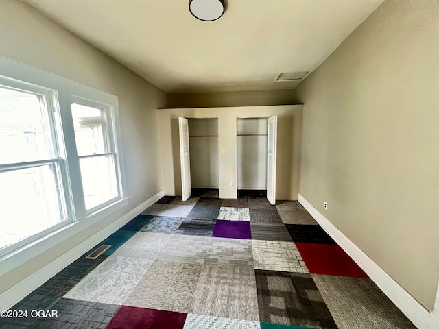 unfurnished bedroom with dark colored carpet, multiple windows, and two closets