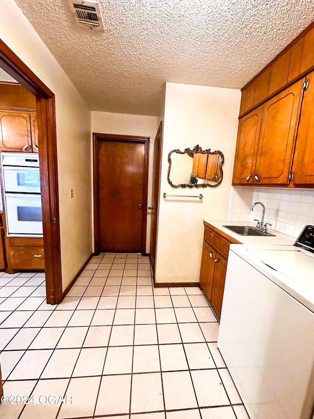 kitchen featuring white double oven, backsplash, sink, light tile patterned floors, and washer / dryer