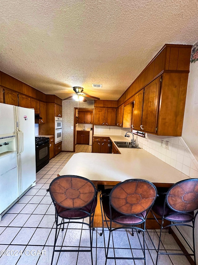 kitchen with white appliances, backsplash, sink, a textured ceiling, and kitchen peninsula