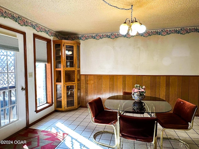 dining space featuring wooden walls, light tile patterned floors, a textured ceiling, and an inviting chandelier