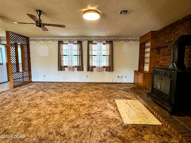 unfurnished living room with carpet flooring, a wood stove, ceiling fan, and a textured ceiling