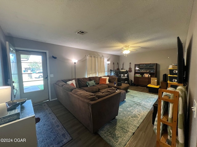 living room featuring dark wood-type flooring, ceiling fan, and a textured ceiling