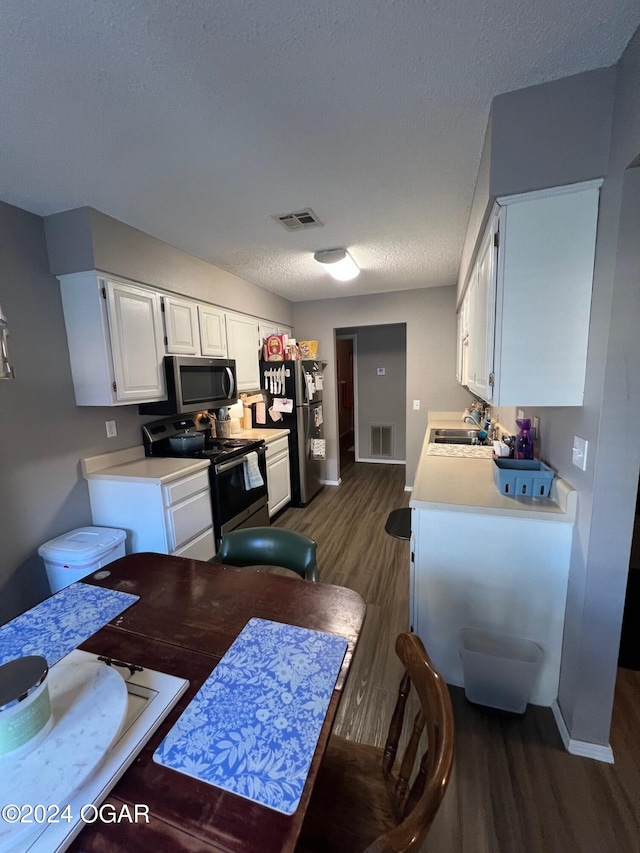 kitchen featuring dark wood-type flooring, white cabinets, a textured ceiling, and stainless steel appliances