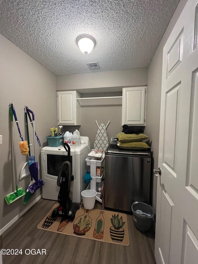 laundry area featuring a textured ceiling, dark hardwood / wood-style flooring, cabinets, and washing machine and clothes dryer