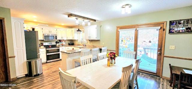 kitchen with stainless steel appliances, hardwood / wood-style flooring, a kitchen breakfast bar, white cabinetry, and decorative light fixtures