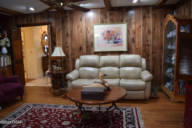 living room with ceiling fan, wooden walls, beamed ceiling, and light wood-type flooring