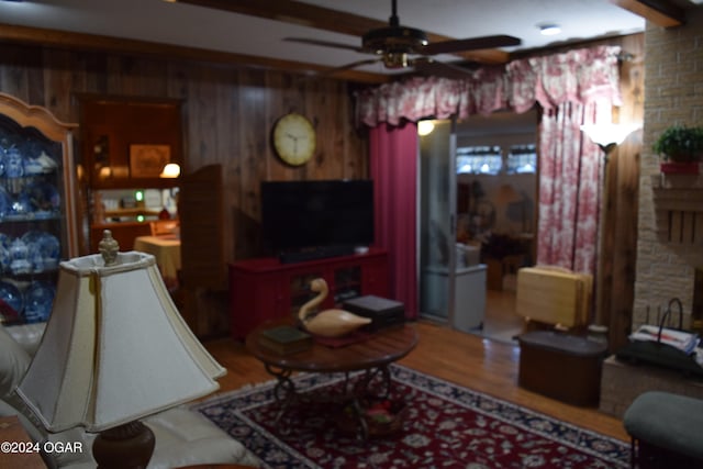 living room featuring beam ceiling, ceiling fan, wood-type flooring, and wood walls