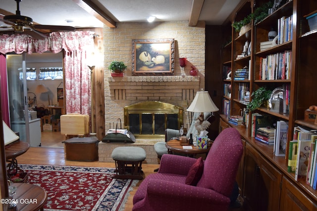 sitting room with a brick fireplace, ceiling fan, a textured ceiling, beamed ceiling, and wood-type flooring