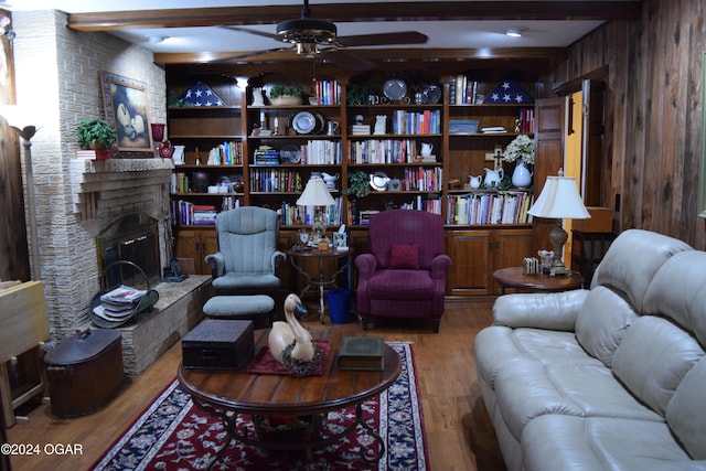 living room featuring ceiling fan, a brick fireplace, beamed ceiling, wood walls, and wood-type flooring