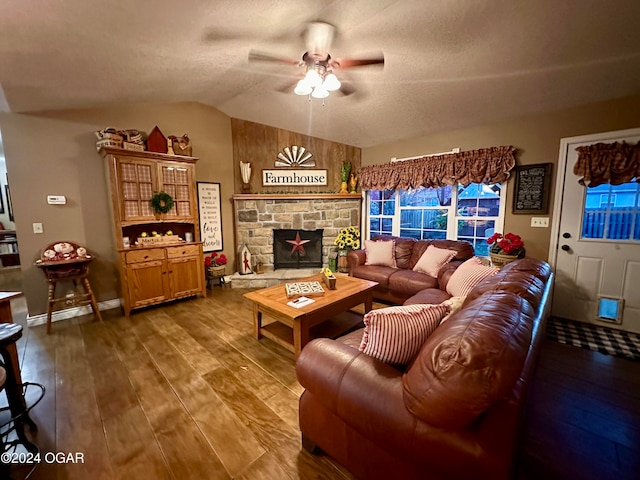 living room featuring ceiling fan, a stone fireplace, a textured ceiling, vaulted ceiling, and hardwood / wood-style flooring