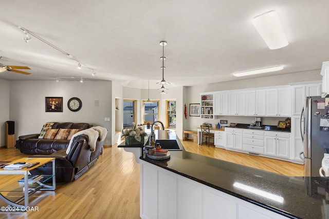 kitchen featuring stainless steel fridge, light wood-type flooring, sink, decorative light fixtures, and white cabinetry