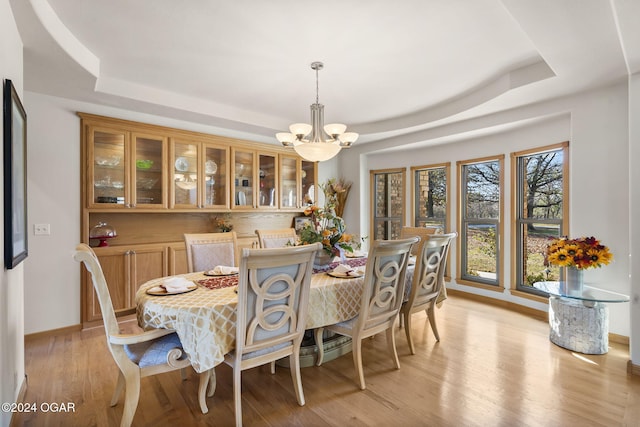 dining room featuring a notable chandelier, light hardwood / wood-style floors, and a tray ceiling