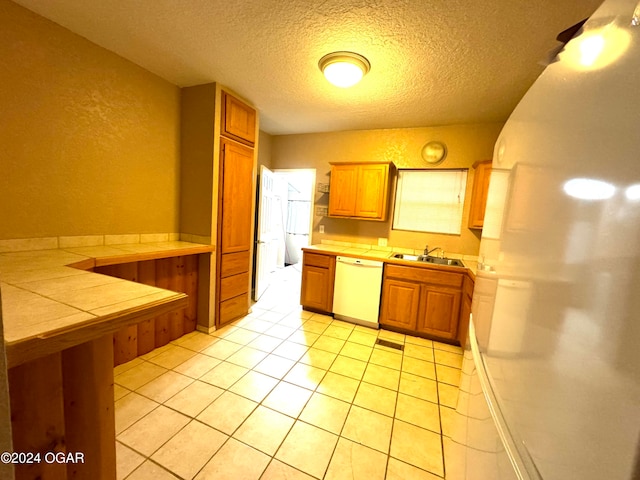 kitchen featuring tile counters, sink, white dishwasher, a textured ceiling, and light tile patterned floors