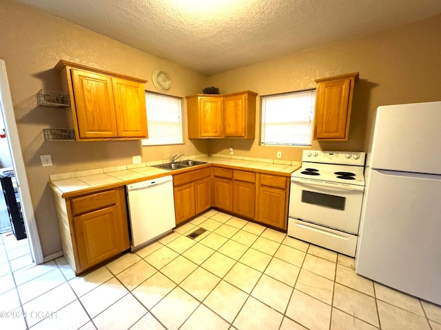 kitchen with tile countertops, white appliances, sink, light tile patterned floors, and a textured ceiling