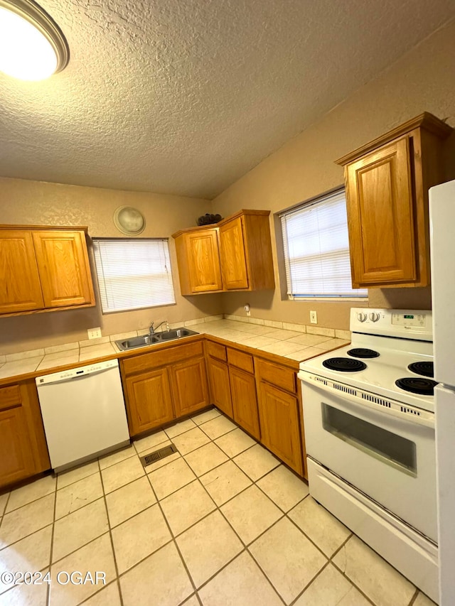 kitchen featuring white appliances, sink, light tile patterned floors, a textured ceiling, and tile counters