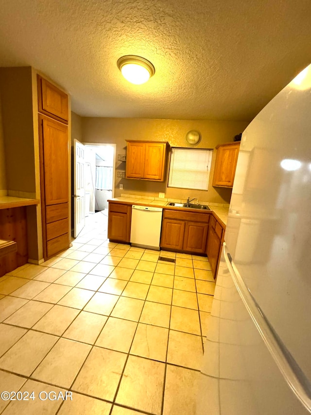 kitchen featuring a textured ceiling, white appliances, light tile patterned floors, and sink