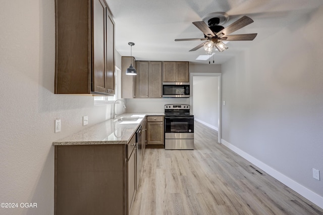 kitchen featuring light stone countertops, appliances with stainless steel finishes, sink, light hardwood / wood-style floors, and hanging light fixtures