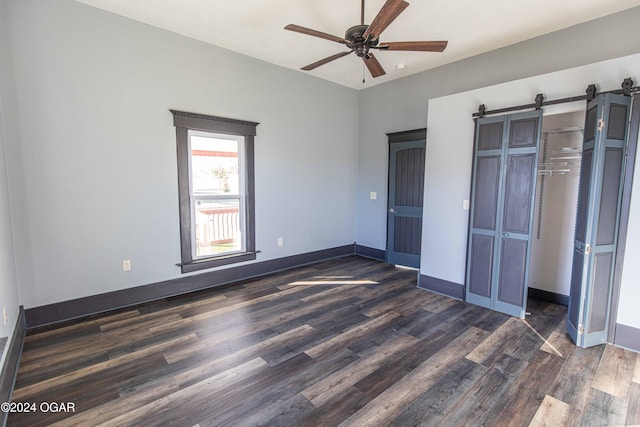 unfurnished bedroom featuring a barn door, a closet, ceiling fan, and dark wood-type flooring