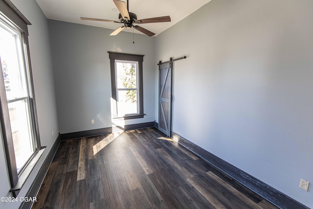 unfurnished room with a barn door, dark hardwood / wood-style floors, and ceiling fan