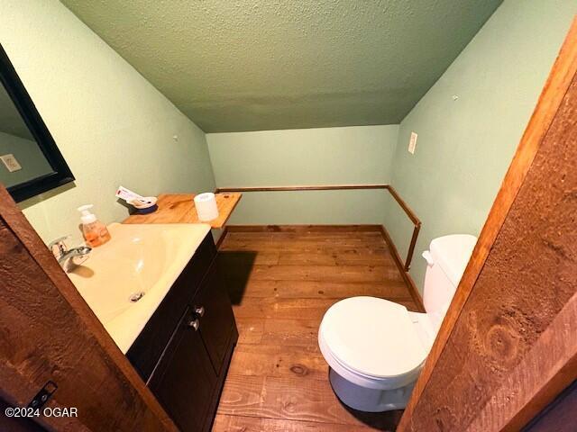 bathroom with wood-type flooring, lofted ceiling, a textured ceiling, toilet, and vanity