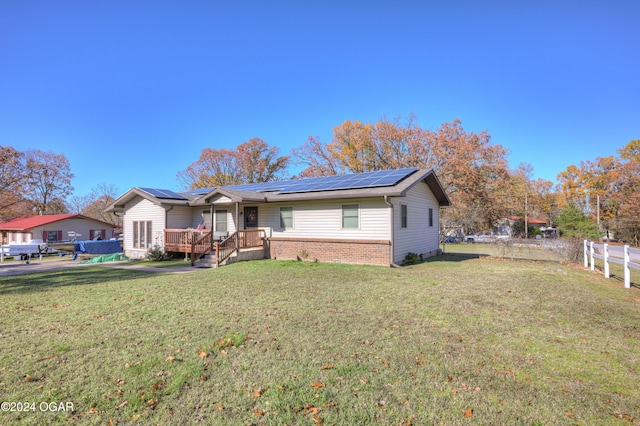 ranch-style home with a front yard, solar panels, and a wooden deck