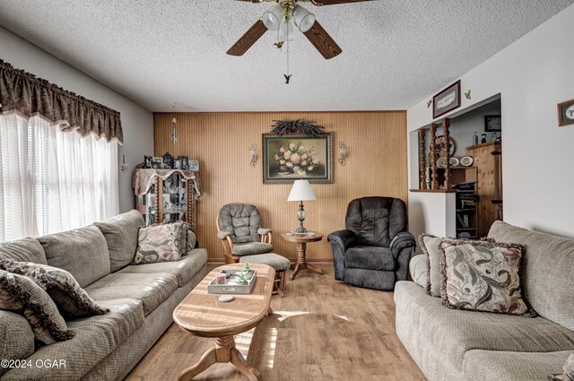 living room featuring a textured ceiling, light hardwood / wood-style flooring, ceiling fan, and wood walls