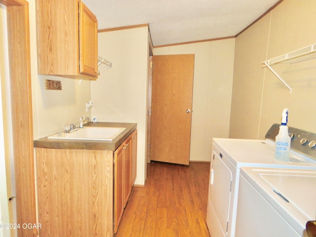 clothes washing area featuring washing machine and clothes dryer, sink, cabinets, crown molding, and light wood-type flooring