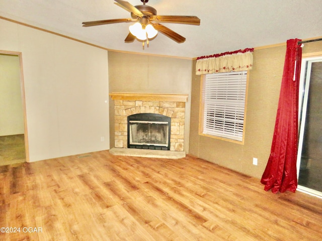 unfurnished living room featuring hardwood / wood-style floors, ceiling fan, a stone fireplace, and ornamental molding