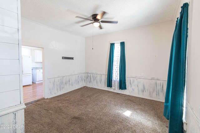 unfurnished room with a textured ceiling, light colored carpet, ceiling fan, and ornamental molding