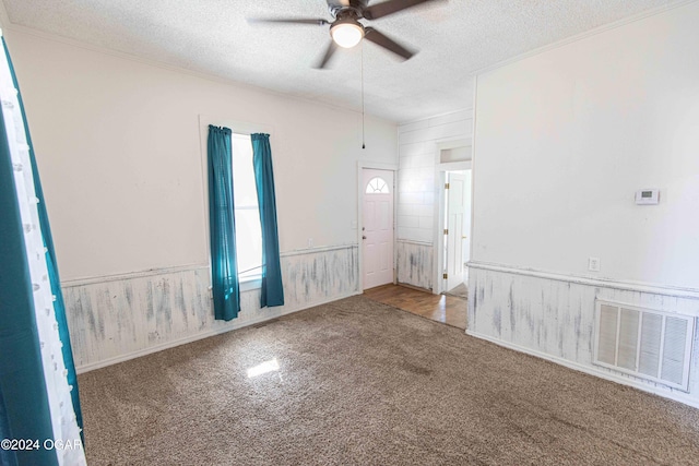 unfurnished room with carpet flooring, ceiling fan, wood walls, and a textured ceiling