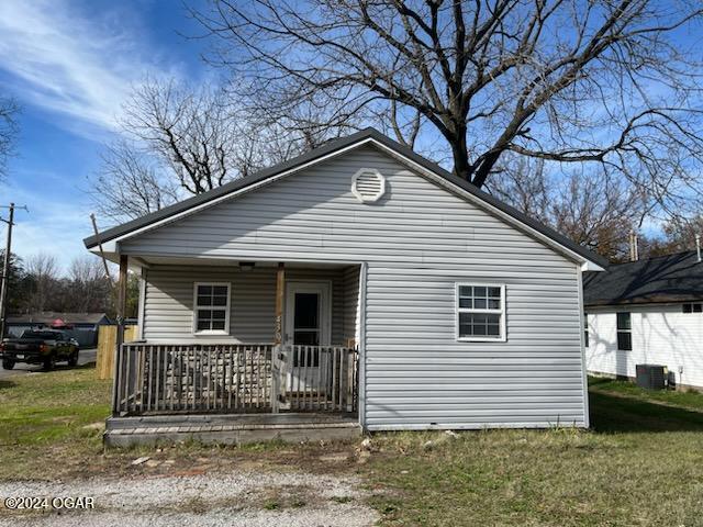 view of front of home featuring covered porch, central AC unit, and a front yard