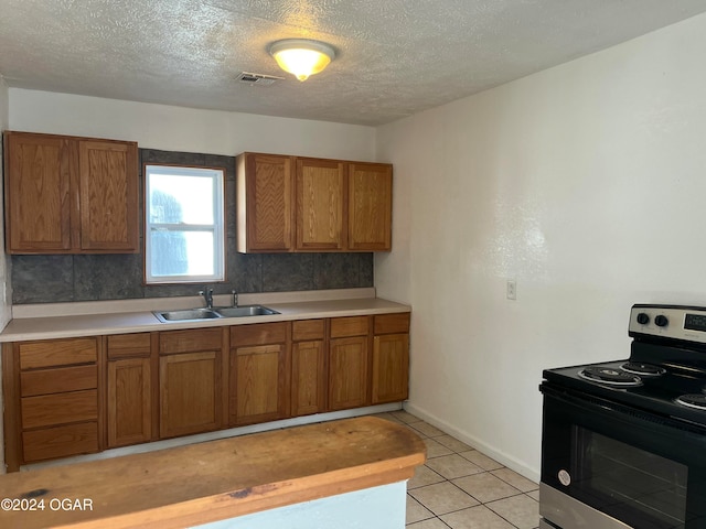 kitchen with stainless steel range with electric cooktop, sink, decorative backsplash, a textured ceiling, and light tile patterned flooring