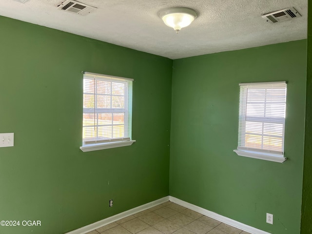 tiled empty room featuring a textured ceiling and a healthy amount of sunlight